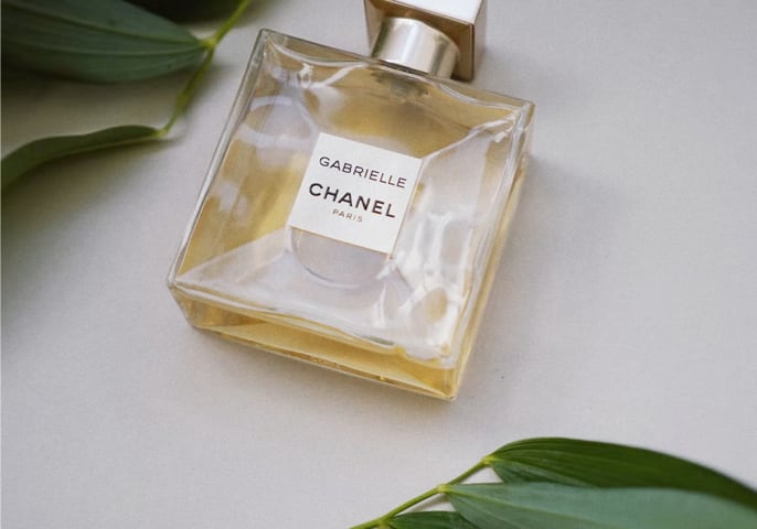 A bottle of perfume surrounded by leafs with a tag reading 'Gabrielle Chanel'.